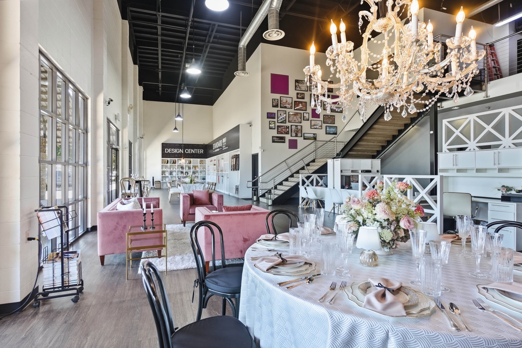 A round table set under a crystal chandelier in the Design Center, with velvet sofas and shelves of tableware behind it.